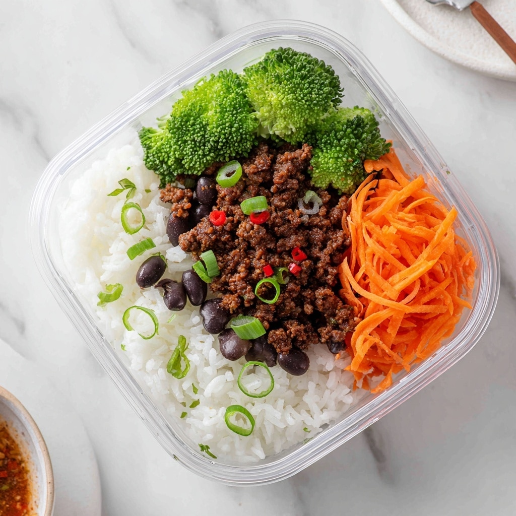 A clear rectangular glass meal prep container with three sections: the bottom layer has white cooked rice, topped in the middle by a layer of dark brown cooked ground meat garnished with white sesame seeds, green onion slices, and red chili slices. On the top left corner, there are bright green steamed broccoli florets, and beside them, on the top right corner, a pile of shredded bright orange carrots. The container is placed on a white marbled surface with part of a metal fork and a small white dish with red sauce visible nearby. Photo taken with an iphone --ar 4:5 --v 7
