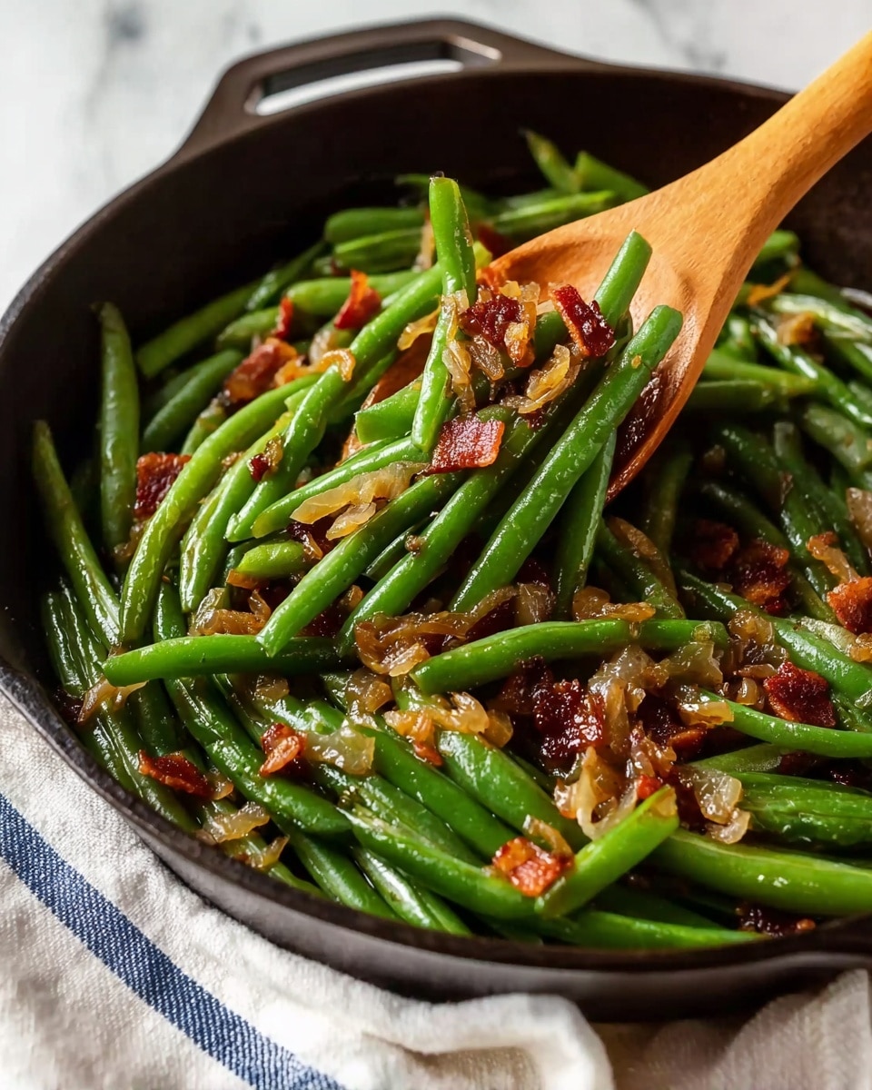 A black cast iron skillet filled with cooked green beans and scattered crispy bacon pieces on top. The green beans are a soft green color, cooked and slightly glossy from moisture, with small bits of translucent cooked onions mixed throughout. The skillet sits on a white marbled textured surface with part of a white and blue striped cloth visible in the background. photo taken with an iphone --ar 4:5 --v 7
