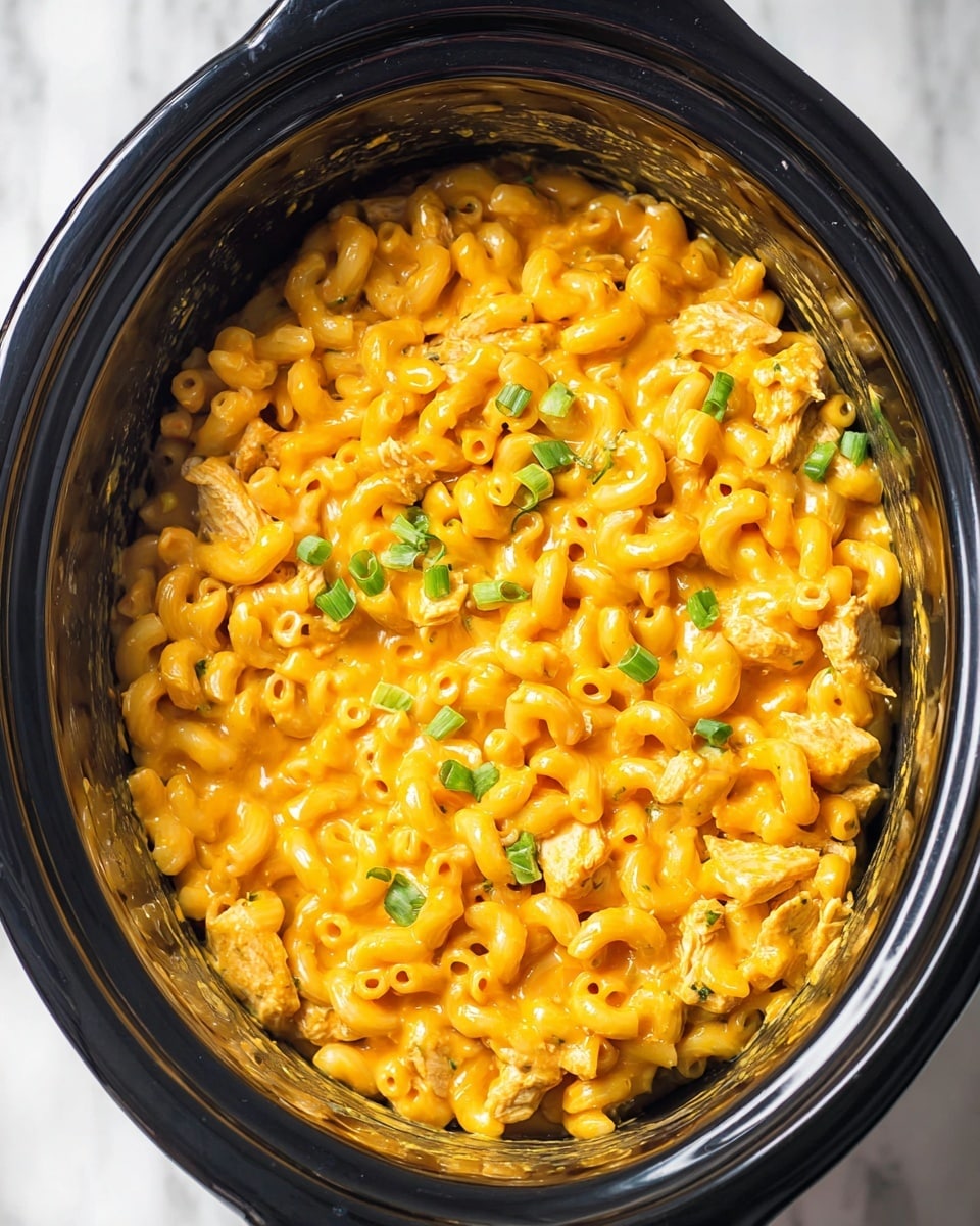 In a black slow cooker, there is a creamy macaroni dish with elbow pasta fully covered in thick, bright orange cheese sauce. Mixed in are small pieces of light brown cooked chicken and scattered green chopped scallions on top. The pasta and sauce mix is glossy and rich, filling most of the cooker, which sits on a white marbled surface. Photo taken with an iphone --ar 4:5 --v 7