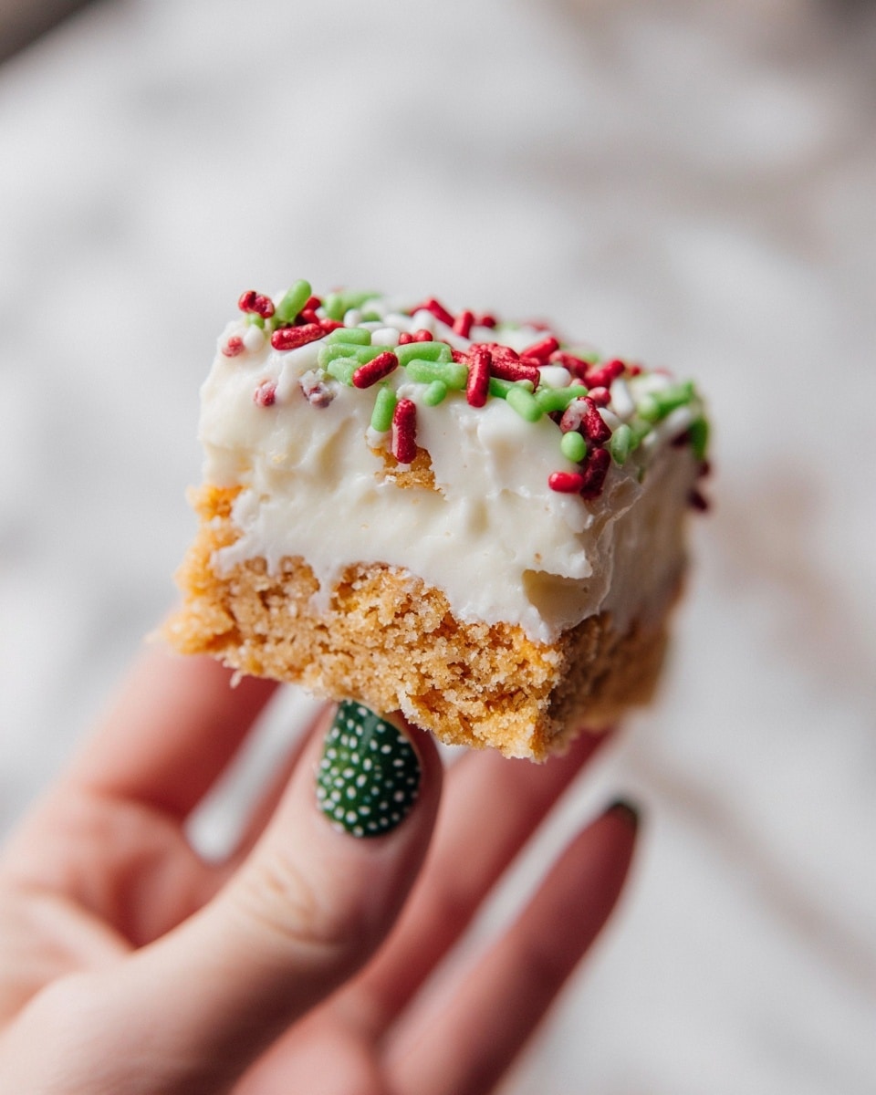 A close-up of a small dessert bar held by a woman's hand with green nail polish with white dots, showing two layers of light brown, crumbly cake separated and topped by a thick, smooth white frosting layer. The sides are covered in the same white frosting with red, green, and white cylindrical sprinkles adding festive colors and texture. The background is a soft-focus white marbled texture. photo taken with an iphone --ar 4:5 --v 7