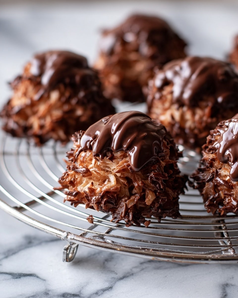 A close-up of several round chocolate coconut clusters on a silver wire cooling rack, each cluster covered with rough-textured shredded coconut coated in dark brown chocolate, and topped with a drizzle of smooth, melted chocolate. The clusters are uneven and rustic in shape, with a glossy finish on the chocolate parts. The rack is placed on a white marbled surface. photo taken with an iphone --ar 4:5 --v 7