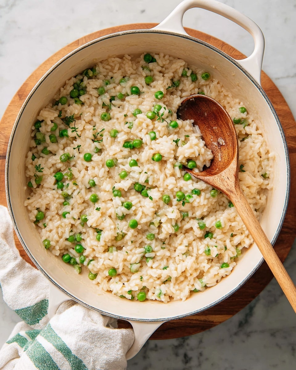A large white pot filled with creamy, light beige risotto mixed evenly with bright green peas, showing a soft and slightly glossy texture. A wooden spoon with a smooth surface rests inside the pot, partially stirring the risotto, revealing the thick and slightly loose consistency of the rice dish. The pot is placed on a round wooden board, sitting on a white marbled surface, with a white cloth with green stripes lying nearby. The overall scene looks warm and inviting with a homemade feel. photo taken with an iphone --ar 4:5 --v 7