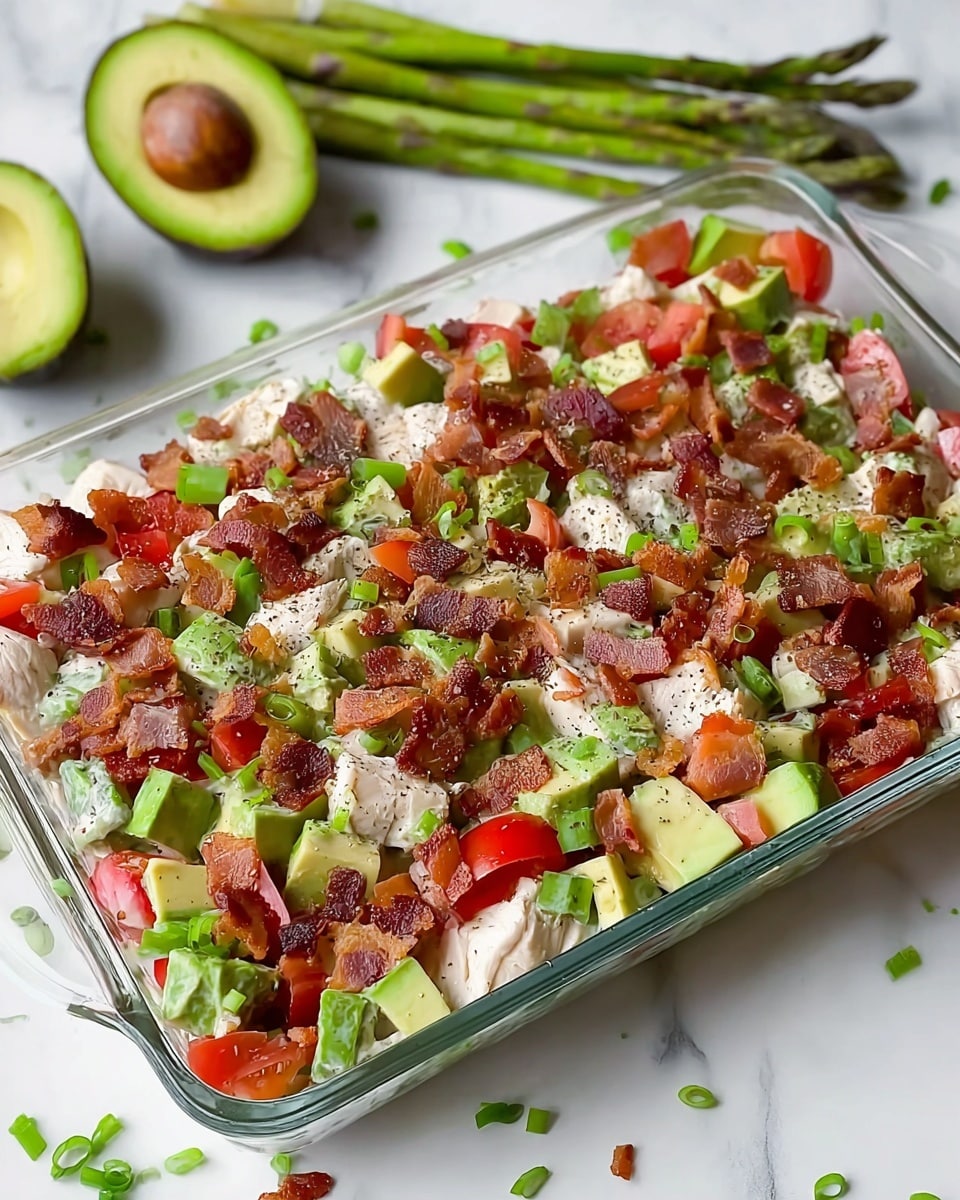 The image shows a clear rectangular glass dish filled with a mixed salad. The salad layers are even, with chunks of light green avocado, red tomato pieces, crispy dark brown bacon bits, and white chicken pieces spread evenly throughout. Small bright green chopped scallions are scattered on top along with a light sprinkling of black pepper. Behind the dish, there is a halved avocado and some asparagus placed on a white marbled surface, giving a fresh and clean look. photo taken with an iphone --ar 4:5 --v 7