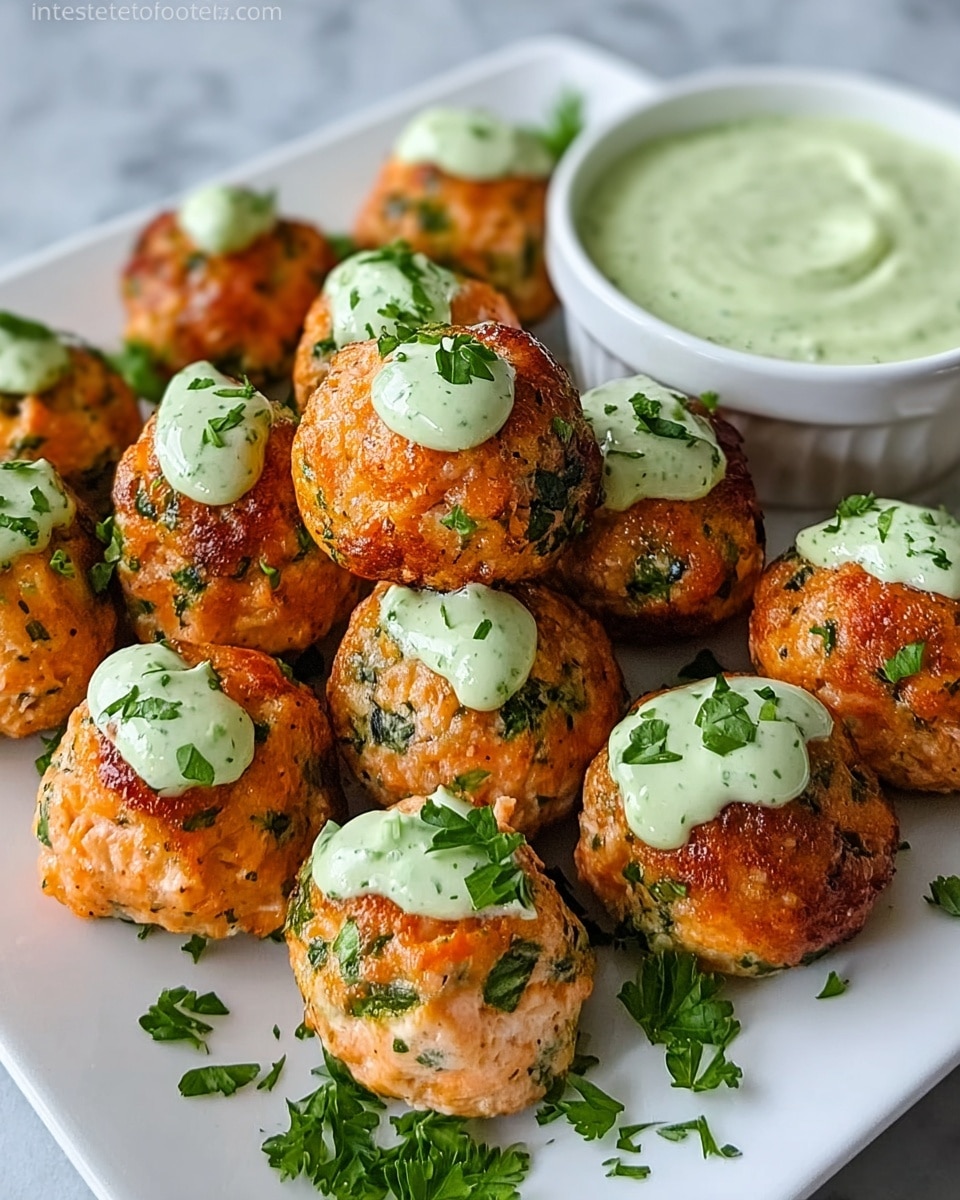 The image shows a white square plate with two layers of round salmon balls, about twelve in total. Each salmon ball is golden brown with green herb bits mixed throughout, giving a textured look. On top of many salmon balls, there is a dollop of pale green creamy sauce with small green herb specks. The salmon balls are also sprinkled with fresh chopped parsley leaves around the plate. At the back right corner, there is a white bowl filled with the same pale green sauce. The plate is placed on a white marbled surface. photo taken with an iphone --ar 4:5 --v 7