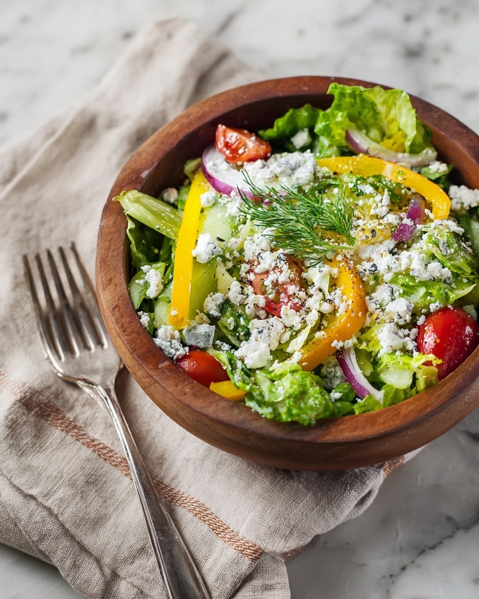 The image shows a fresh salad in a round wooden bowl with visible layers of ingredients. The bottom layer is bright green romaine lettuce leaves, roughly torn. On top of the greens, there are slices of yellow and red tomatoes, along with translucent rounds of white onion. Scattered across the salad are creamy white dollops of goat cheese, and small green dill sprigs add a fresh garnish. Light yellow seeds, possibly chopped nuts or grains, are sprinkled throughout the salad, giving it texture. The bowl sits on a white marbled surface with a beige and brown cloth underneath, and a silver fork rests nearby. photo taken with an iphone --ar 4:5 --v 7