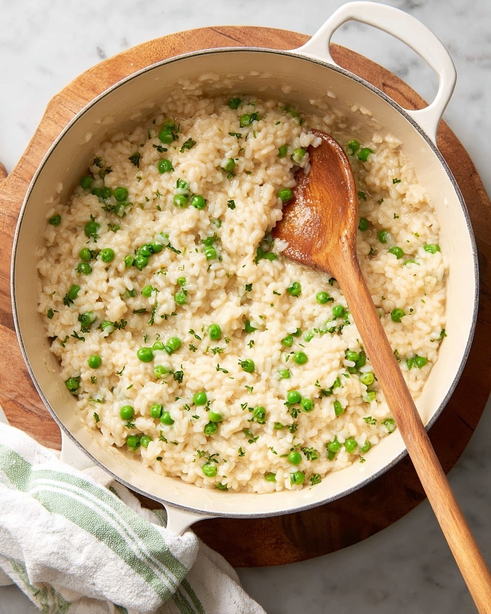 A white pot filled with a creamy risotto that has one main layer of soft, light beige rice mixed evenly with small bright green peas scattered throughout. A wooden spoon is placed inside the pot, partly covered by the risotto on the right side. The pot is sitting on a round wooden board on a white marbled surface. To the side, there is a white cloth with green stripes. photo taken with an iphone --ar 4:5 --v 7