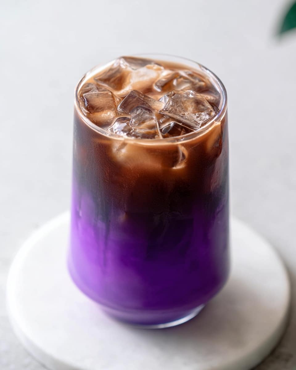 A clear glass holds a two-layered drink, with the bottom layer being a bright purple liquid that is smooth and dense, filling about half the glass. The top layer consists of dark brown iced coffee with visible ice cubes that create a textured, cold appearance. The glass is placed on a round white marble surface that complements the colors of the drink. photo taken with an iphone --ar 4:5 --v 7