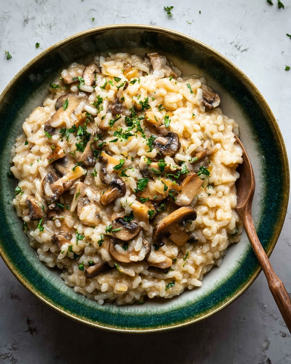 A close-up of a bowl of creamy mushroom risotto in a white bowl with a green inside edge, placed on a white marbled surface. The risotto has several layers: the main layer is creamy off-white rice mixed with small pieces of cooked mushrooms that are light to dark brown. Scattered fresh green herbs are sprinkled on top, adding bright contrast. The dish’s texture looks soft and slightly sticky, with the mushrooms giving it some chunkiness. A wooden spoon rests inside the bowl, ready to scoop, adding warmth to the image. Photo taken with an iphone --ar 4:5 --v 7