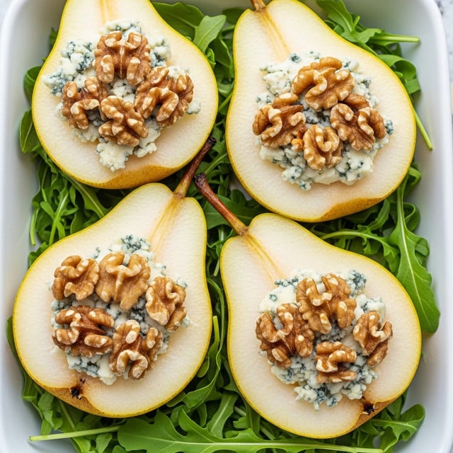 The image shows four halves of pears arranged on a bed of green arugula leaves in a white rectangular dish, each half filled with a layer of creamy blue cheese topped with a cluster of whole walnuts. The pear flesh is light and smooth with the yellowish-green skin that has small brown spots, while the blue cheese adds a crumbly, speckled blue texture, and the walnuts are chunky with a warm brown color. The arugula leaves underneath add a fresh, vibrant green color contrasting with the soft and rich toppings. The photo taken with an iphone --ar 4:5 --v 7