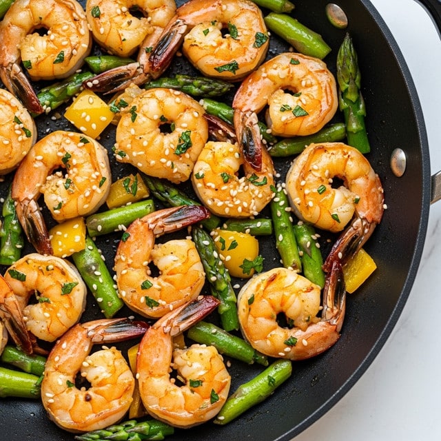 The image shows a close-up of a cooked shrimp dish in a black pan. The dish contains around a dozen plump shrimp, golden-orange in color with slight char marks, mixed with bright green asparagus pieces cut into small sections. There are small pieces of yellow bell pepper scattered throughout, adding a pop of color. The shrimp and vegetables are coated in a glossy sauce with herbs and a sprinkle of white sesame seeds on top. The shrimp tails are visible, and the dish looks juicy and well-seasoned, with hints of green herbs scattered evenly. The pan sits on a white marbled surface. photo taken with an iphone --ar 4:5 --v 7
