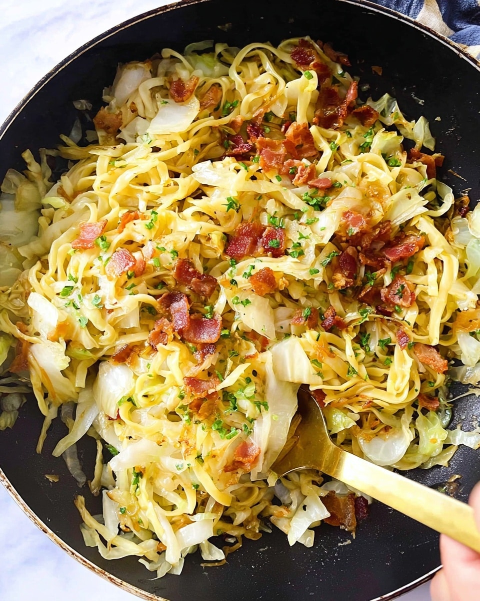 A close-up view of a cooked noodle dish in a black pan, showing soft yellow noodles mixed with slightly browned, thin cabbage pieces that have a crispy texture. Scattered on top are small pieces of crispy reddish-brown bacon. The dish is garnished with finely chopped green herbs, and there is a golden spatula stirring the noodles, held by a woman's hand. The background shows a white marbled surface. photo taken with an iphone --ar 4:5 --v 7