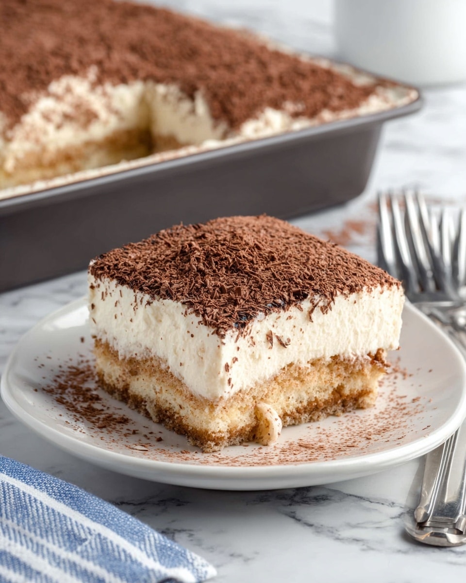 A square piece of cake sits on a white plate with a slightly raised edge, showing three layers: the bottom layer is a light brown, moist sponge cake with a crumbly texture; the middle layer is a thick, creamy white frosting, smooth and dense; the top layer is a fine dusting of dark brown chocolate shavings evenly spread over the frosting. The piece is cut from a rectangular cake in a dark baking pan in the background, with more cake visible inside. The scene is set on a white marbled surface, with two silver forks and a blue and white striped cloth near the plate. Photo taken with an iphone --ar 4:5 --v 7
