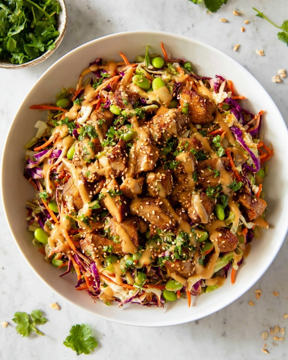 A large white bowl filled with a mixed salad featuring shredded purple and white cabbage as the base layer creating a colorful texture, topped with bright orange shredded carrots and thin red bell pepper slices. The next layer shows chunks of browned meat scattered evenly, with green edamame beans and crunchy peanut pieces spread throughout. Over the salad, a light brown creamy sauce is drizzled generously, garnished with chopped fresh green cilantro and sprinkled white sesame seeds. The bowl sits on a white marbled surface with a small bowl of fresh herbs visible in the background. photo taken with an iphone --ar 4:5 --v 7