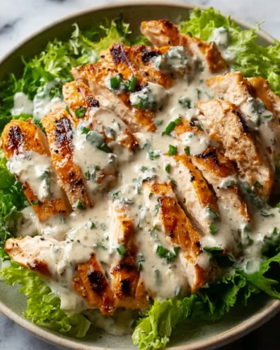 The image shows a white plate with grilled chicken breast slices arranged neatly on a bed of fresh green lettuce leaves. The chicken is golden brown with visible grill marks and is covered in a creamy white sauce that has herbs sprinkled throughout, adding texture and small green specks. The sauce pools slightly around the chicken, making the dish look rich and flavorful. The edges of the plate have a few scattered herbs for decoration. The background is a white marbled texture. Photo taken with an iphone --ar 4:5 --v 7
