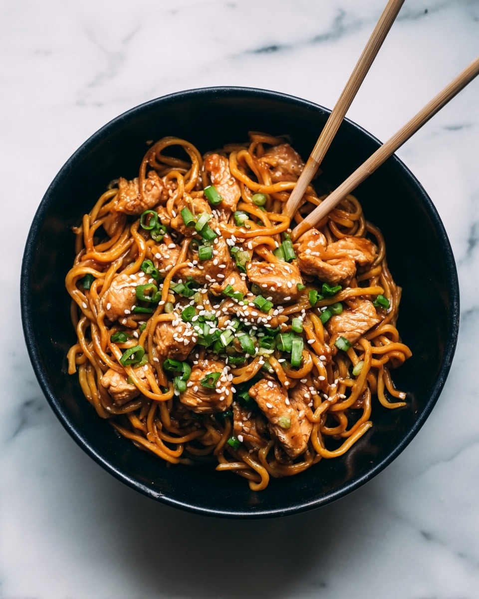 A black bowl filled with a layer of glossy orange-brown cooked noodles at the bottom, topped with chunks of shiny brown glazed chicken pieces, sprinkled with bright green chopped scallions and small white sesame seeds, with a pair of light beige chopsticks resting inside the bowl. The bowl sits on a white marbled surface. photo taken with an iphone --ar 4:5 --v 7