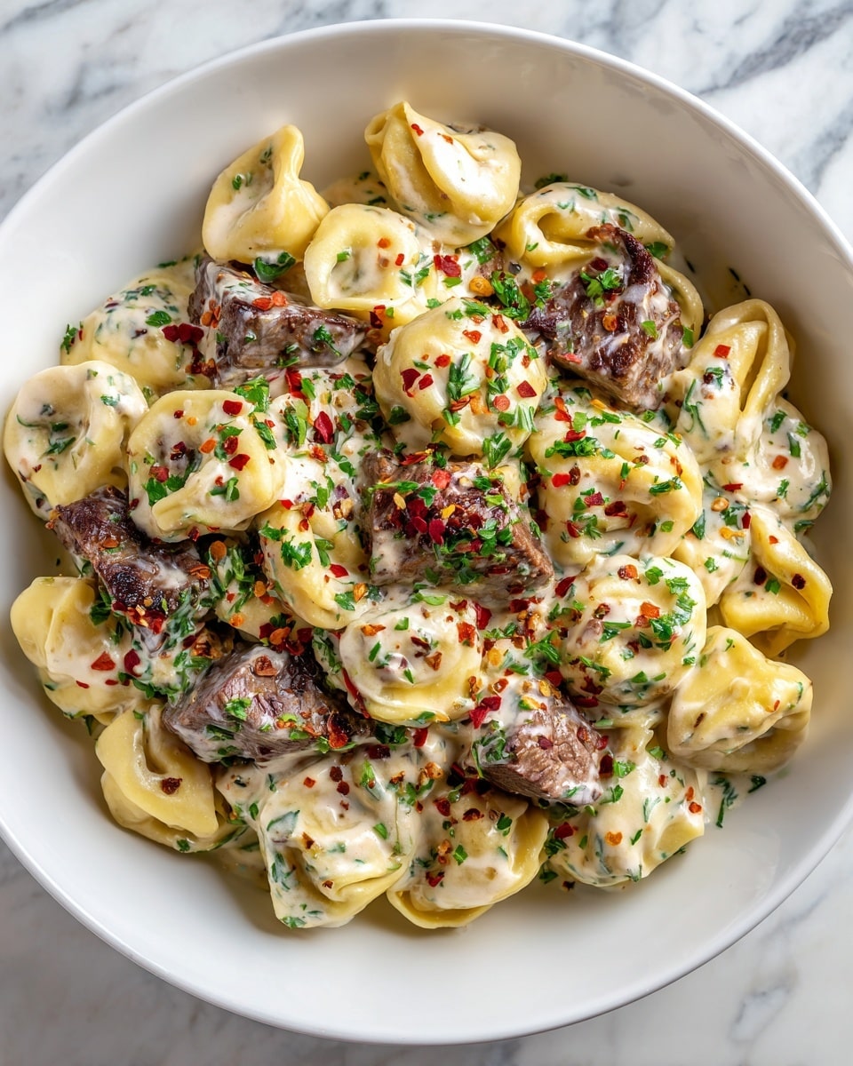 The image shows a white plate filled with creamy tortellini pasta, each piece stuffed and covered in a smooth, white sauce. On top, there are several chunks of dark brown grilled steak scattered evenly across the dish. The tortellini have a soft, slightly folded texture, and the sauce looks rich and thick, coating each piece. Small green herbs and red chili flakes are sprinkled over the meal, adding a touch of color and freshness. The plate sits on a white marbled surface, and a woman's hand is gently holding the edge of the plate. Photo taken with an iphone --ar 4:5 --v 7