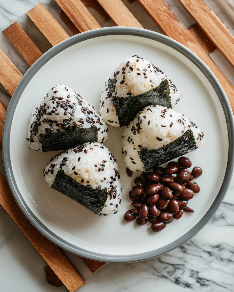 Three triangular onigiri rice balls are arranged in a slight diagonal line on a white plate with a thin dark rim. Each rice ball has a base layer of white sticky rice sprinkled with small dark green seaweed flakes and wrapped partially at the bottom with a rectangular strip of dark green seaweed. Next to the rice balls on the plate is a pile of glossy, caramel-brown simmered beans. The plate sits on a wooden slatted surface with a white marbled texture background. photo taken with an iphone --ar 4:5 --v 7
