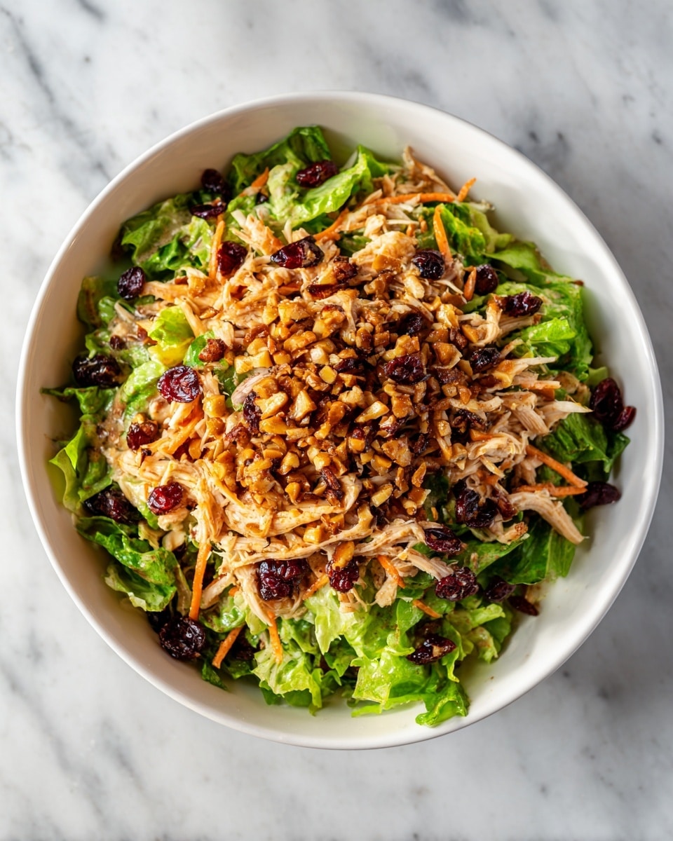 A white bowl filled with a three-layer salad sits on a white marbled surface. The bottom layer is fresh, bright green leafy lettuce. The middle layer features shredded light beige chicken pieces. The top layer is a mix of small, dark red berries, thin strips of orange carrot, and chopped brown nuts scattered all over. The salad looks fresh with a soft natural light shining from the side. photo taken with an iphone --ar 4:5 --v 7