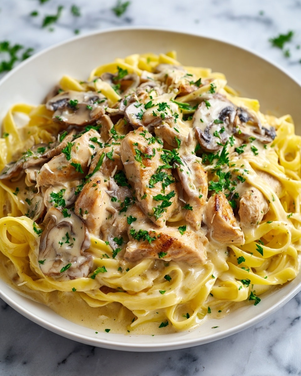 A white plate filled with creamy fettuccine pasta, coated in a thick white sauce mixed with small pieces of mushrooms. On top, there is sliced grilled chicken with light brown grill marks, and the whole dish is sprinkled with chopped green herbs. The textures show the smooth sauce, tender pasta strands, and firm chicken slices, all arranged closely together. The photo is taken on a white marbled surface. photo taken with an iphone --ar 4:5 --v 7