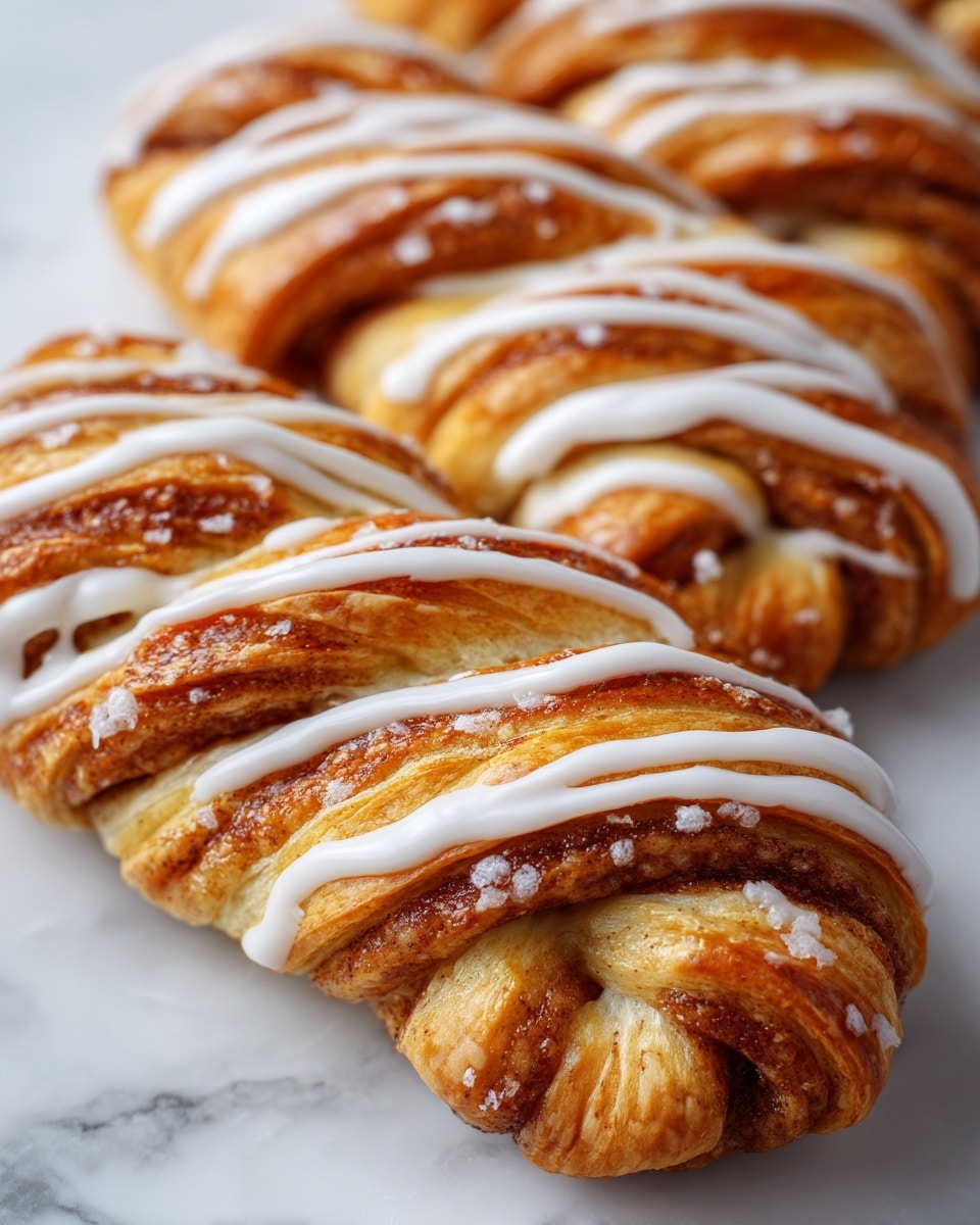 A close-up of a twisted cinnamon pastry with a golden brown crust showing layers of soft, fluffy dough and cinnamon filling. The pastry is drizzled with white icing across the top, adding a shiny texture. The background is a white marbled surface, making the warm colors of the pastry stand out. Photo taken with an iphone --ar 4:5 --v 7