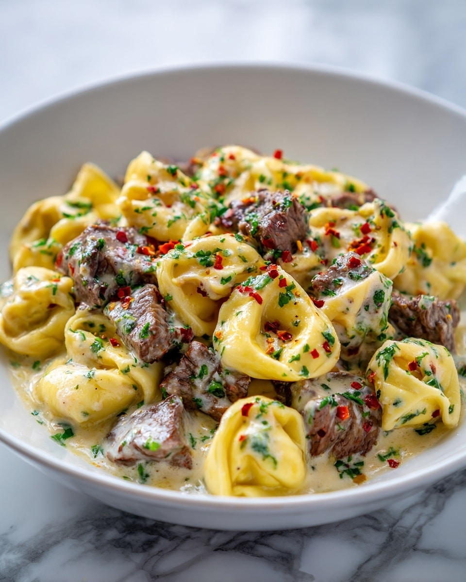 The image shows a white bowl filled with creamy tortellini pasta mixed with pieces of cooked beef. The tortellini are a pale yellow color with a smooth, soft texture, while the beef chunks are dark brown with a slightly charred outer layer. The dish is covered in a rich creamy white sauce speckled with finely chopped green herbs and red pepper flakes. The bowl is placed on a white marbled surface. Photo taken with an iphone --ar 4:5 --v 7