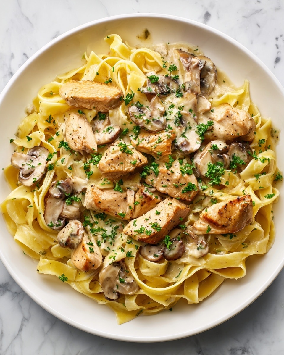 A white plate filled with creamy fettuccine pasta layered at the bottom, coated in a smooth, pale yellow sauce. On top, there are evenly spread pieces of light brown cooked chicken breast and soft, sliced mushrooms mixed into the sauce. The dish is sprinkled with finely chopped green parsley for a touch of color. The background is a white marbled surface. photo taken with an iphone --ar 4:5 --v 7
