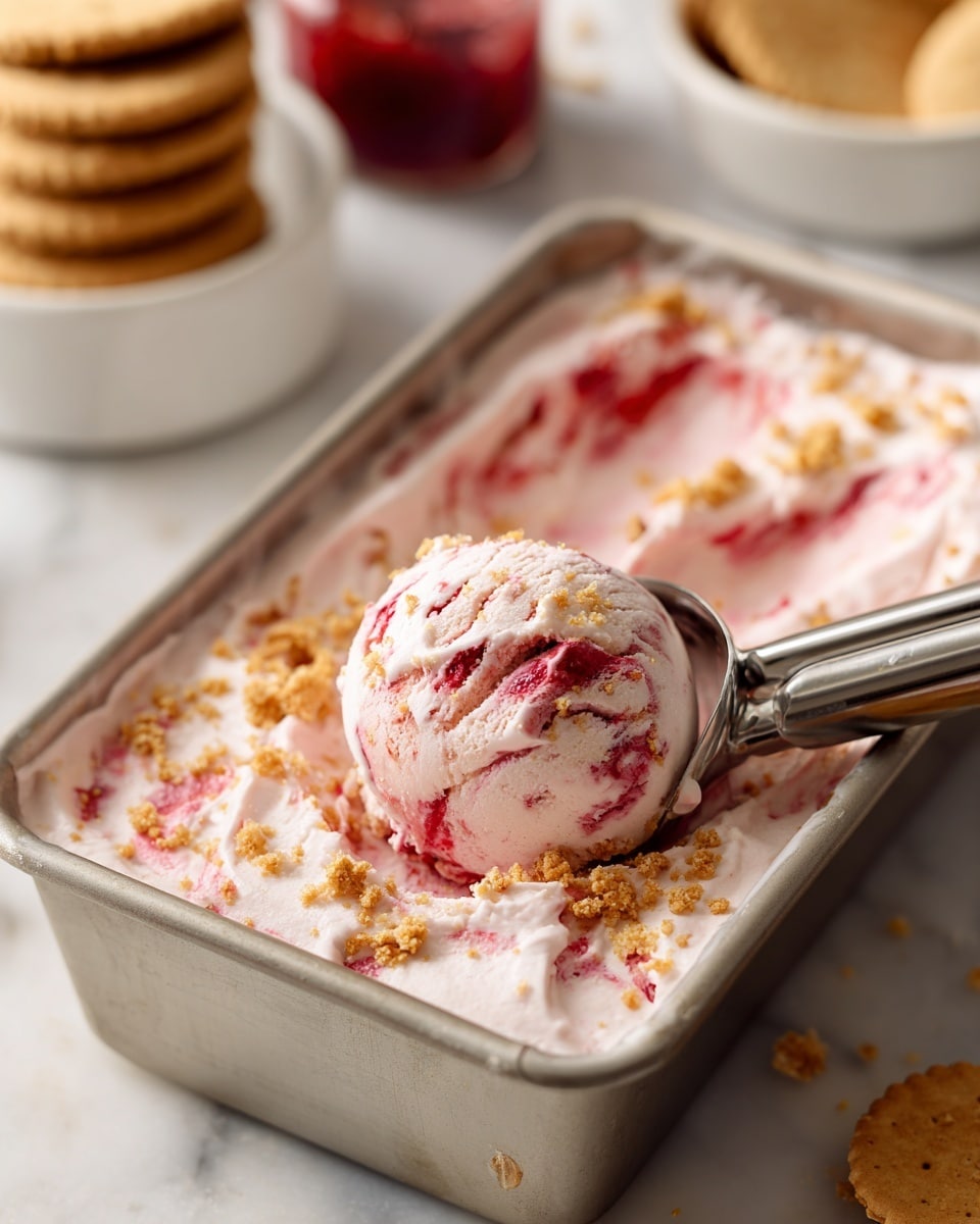 The image shows a metal loaf pan filled with creamy white ice cream that has swirls of deep red fruit sauce throughout. On top of the ice cream, there are small bits of light brown crumb toppings scattered. A scoop of the ice cream is held above the pan with a silver ice cream scoop, showing a mix of the white ice cream, red swirls, and brown crumb pieces. The background consists of a white marbled surface with blurred elements including a small white bowl holding rectangular biscuits and a small jar with red sauce. photo taken with an iphone --ar 4:5 --v 7