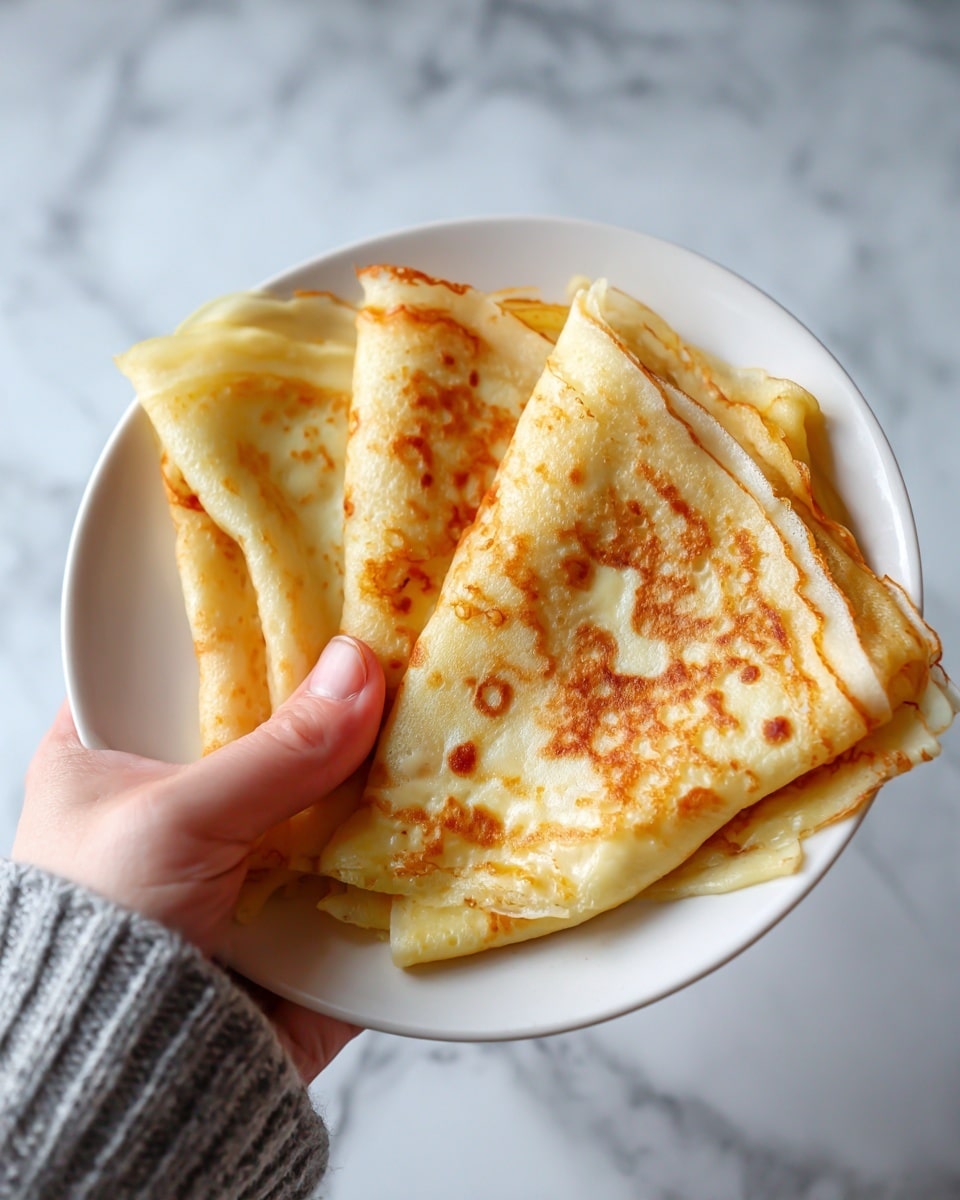 A folded crepe resting on a white plate, showing a golden-brown, slightly crispy outer layer with darker browned spots. The edges are thin and lightly curled, revealing a soft, light cream filling inside. The crepe is thick enough to hold the filling but still looks delicate with a smooth texture. The background is a white marbled surface with soft natural light illuminating the dish. Photo taken with an iphone --ar 4:5 --v 7