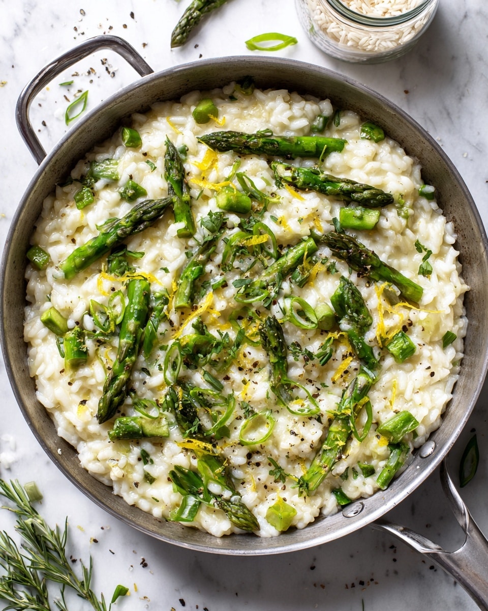 The image shows a close-up of creamy risotto with bright green asparagus pieces mixed in and scattered on top. The risotto has a thick texture with visible grains of rice coated in a light beige sauce. The asparagus is cut into both whole tips and smaller chunks, giving a fresh, vibrant green contrast to the dish. Freshly chopped green herbs and a sprinkle of black pepper are visible on the surface. The risotto is inside a silver pan placed on a white marbled surface, next to a jar of rice and some loose green herbs. photo taken with an iphone --ar 4:5 --v 7
